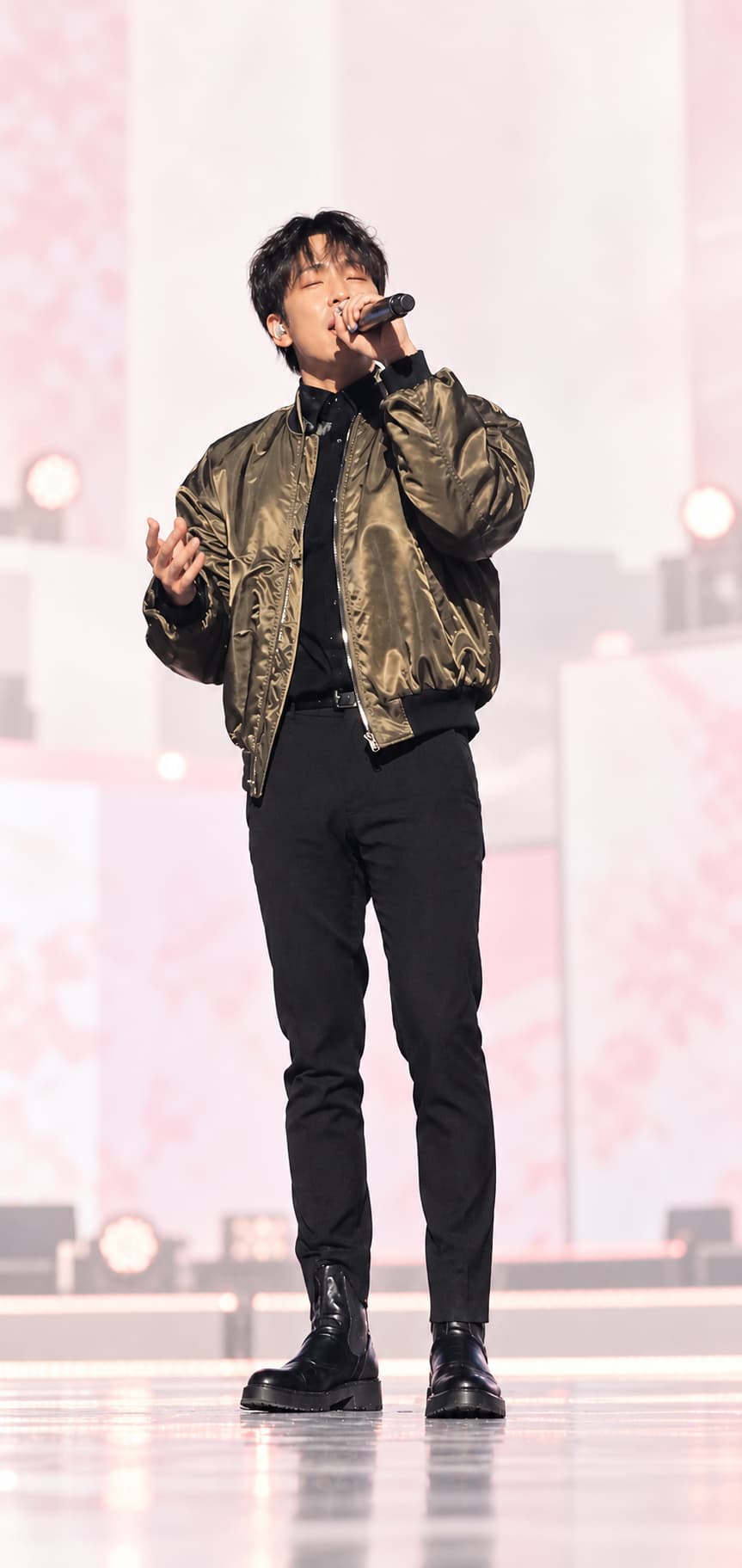 Soft, low-resolution phone photo of a fictional pop vocalist on stage